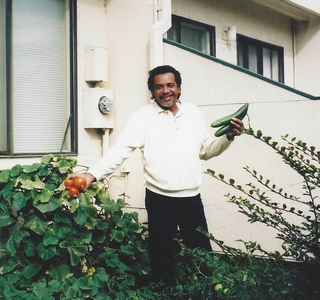 A man is standing outside of house holding a zucchini 