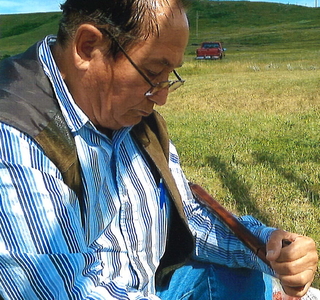 Joe W. Azure sitting in grass smoking pipe at pipe ceremony