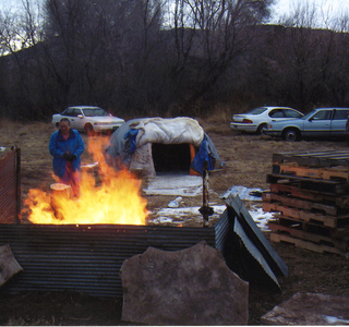 A group of men standing around a fire at sweat lodge and supporters reunion in 2002